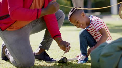 Happy-african-american-father-and-son-pitching-tent-in-sunny-garden,-in-slow-motion