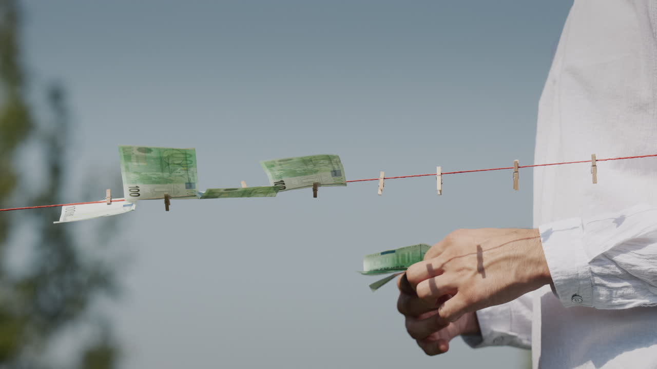 A man's hand removes euro banknotes from a clothesline. Corruption and money laundering concept