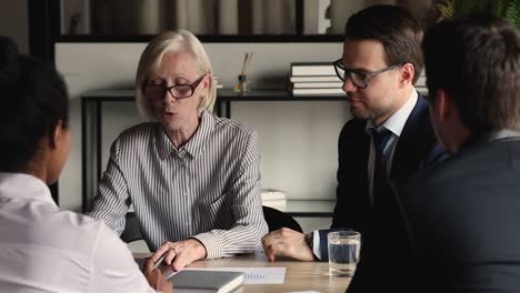 confident older senior businesswoman negotiating strategy with diverse colleagues.