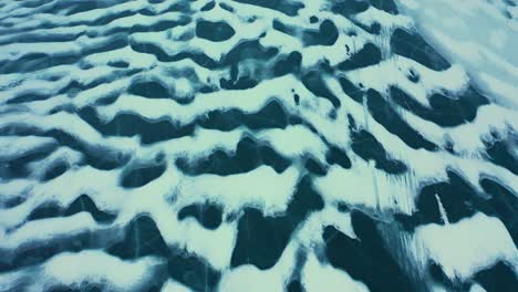 top down aerial shot flying backwards over the wind swept patterns of snow on a frozen lake