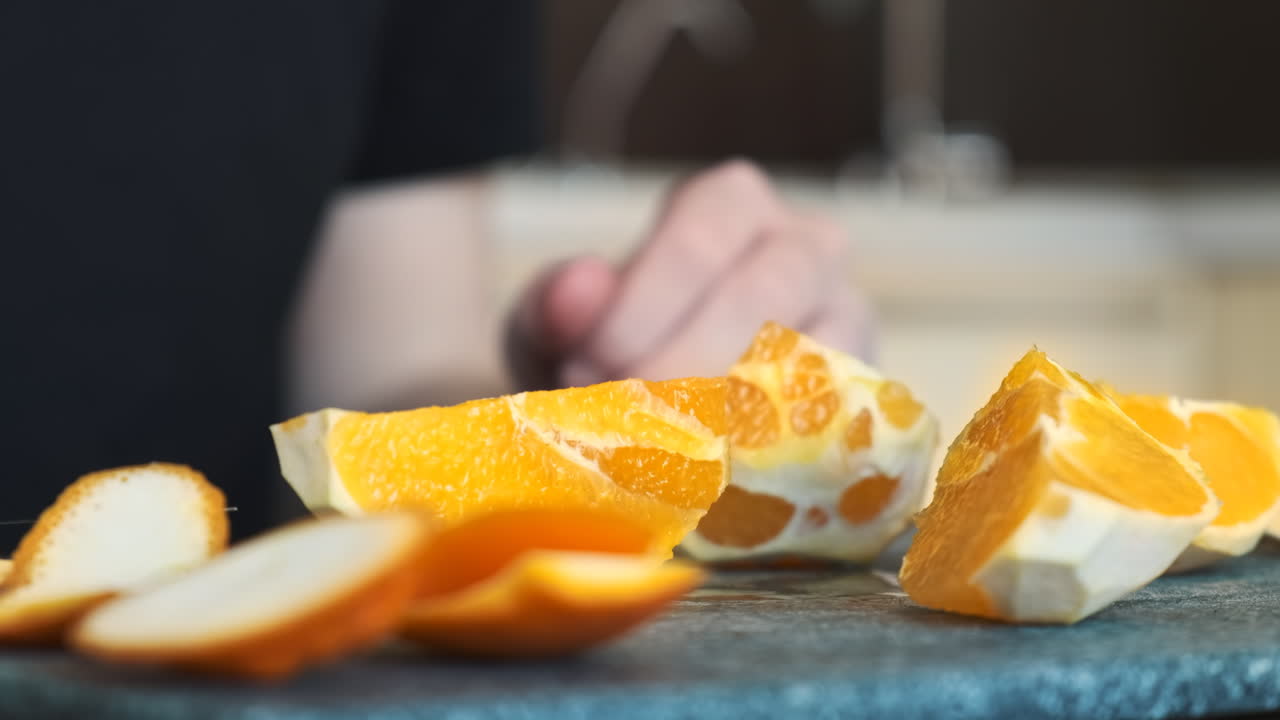 A man slicing an orange on a cooking board using a knife