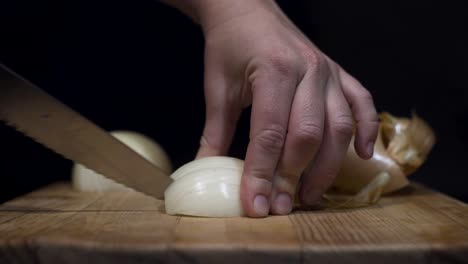 close up shot of lady cutting onions on cutting board with black background