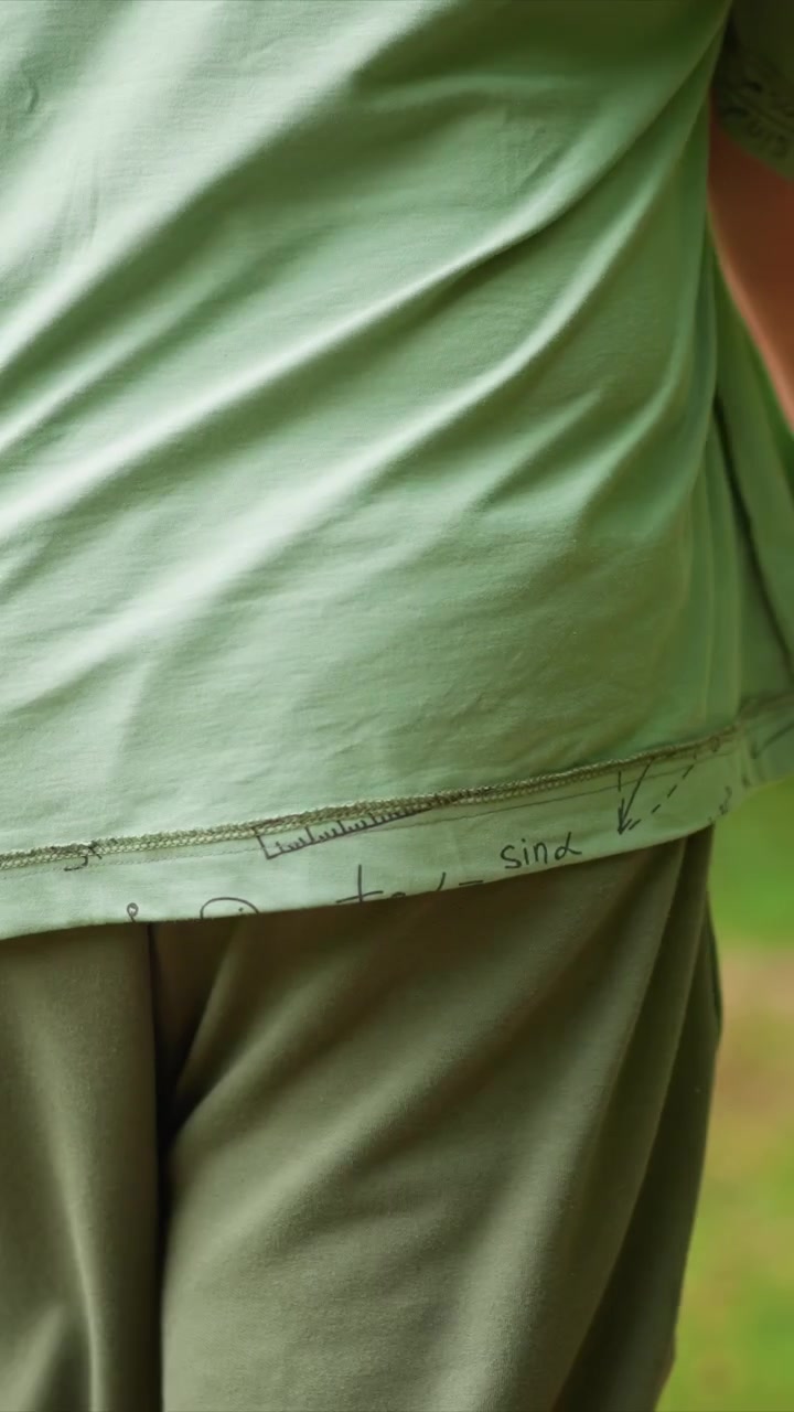 Mid torso view of someone wearing math drawn T shirt. Mathematical notations including trigonometric symbols. Greenery forms indistinct backdrop for close up view focused