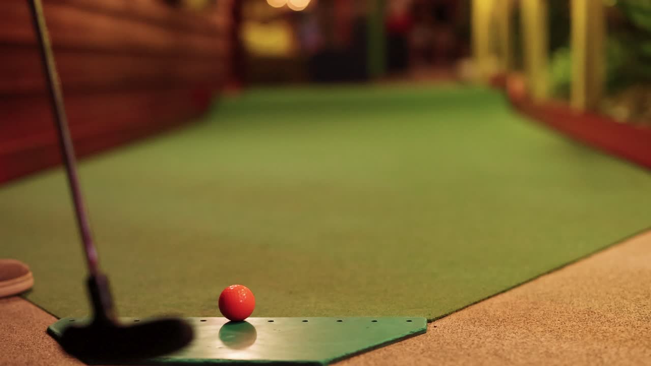A golfer putts a ball on a miniature golf course at night, aiming for precision on a green ramp