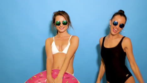 dos mujeres en trajes de baño posando con gafas de sol y flotador de rosquillas