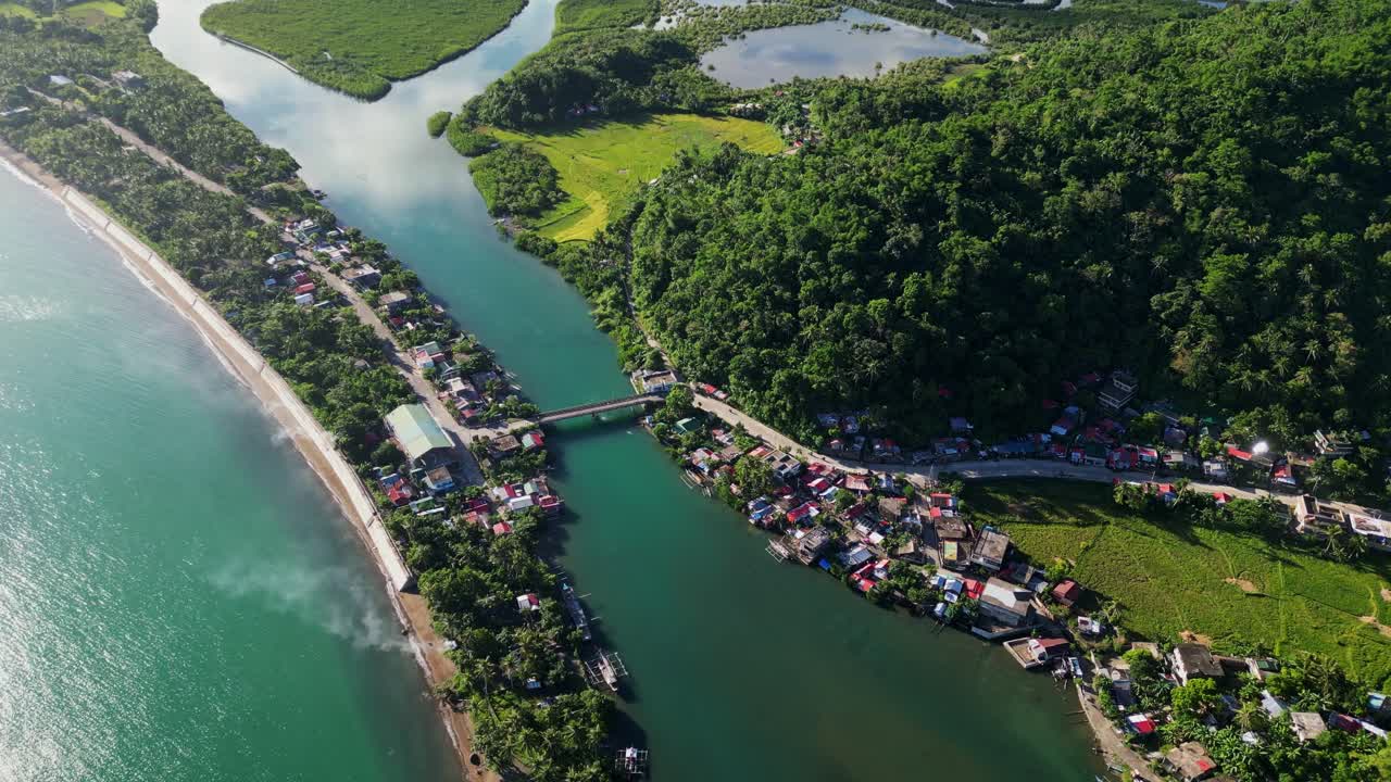 Lush tropical island barangay town, Batalay, with quaint homes, winding roads and bridge, coastal ocean waters, and mangrove river - aerial drone shot
