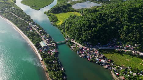 lush tropical island barangay town, batalay, with quaint homes, winding roads and bridge, coastal ocean waters, and mangrove river - aerial drone shot