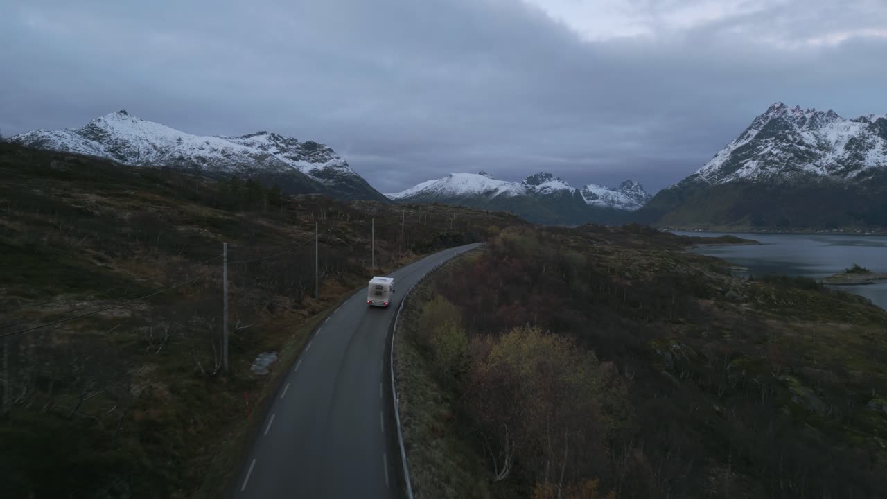 Twilight descends on Lofoten's road with a camper van amidst snowy peaks