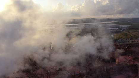 Drohnenaufnahme-Einer-Kohle--Und-Metallfabrik-Bei-Sonnenaufgang,-Die-Durch-Große-Dampfschornsteine-In-Betrieb-Fliegt