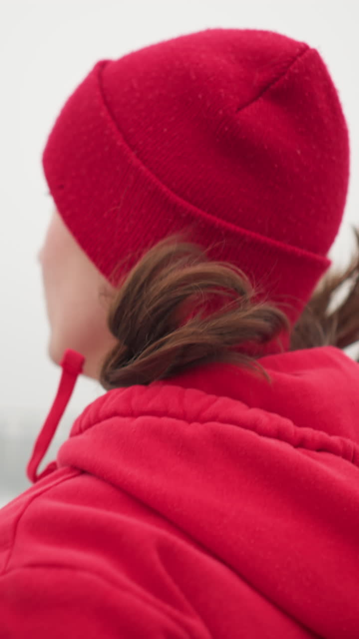 close up of woman in red beanie and hoodie jogging outdoors during winter near iron railing by bridge in foggy atmosphere showcasing fitness and active lifestyle in serene urban surroundings