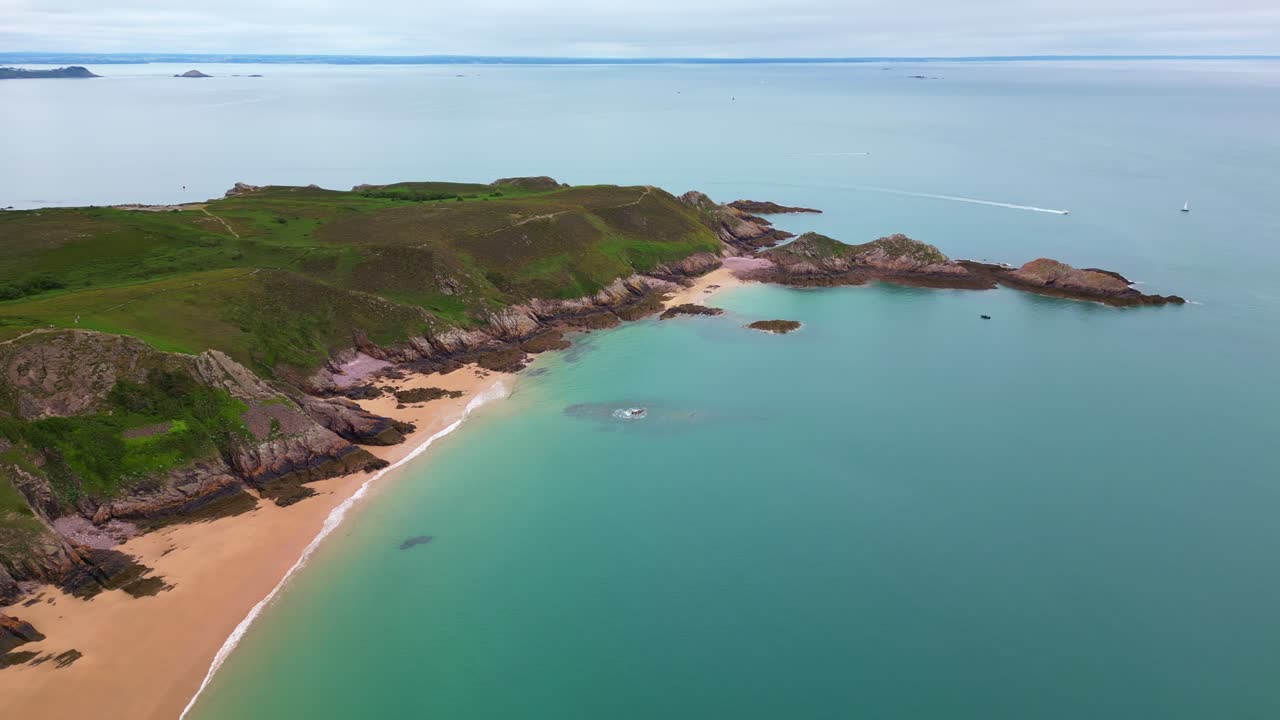 Aerial drone view of the idyllic Plage de Lourtuais beach, the rocky peninsula of Cap d'Erquy, and calm turquoise sea in Brittany, France