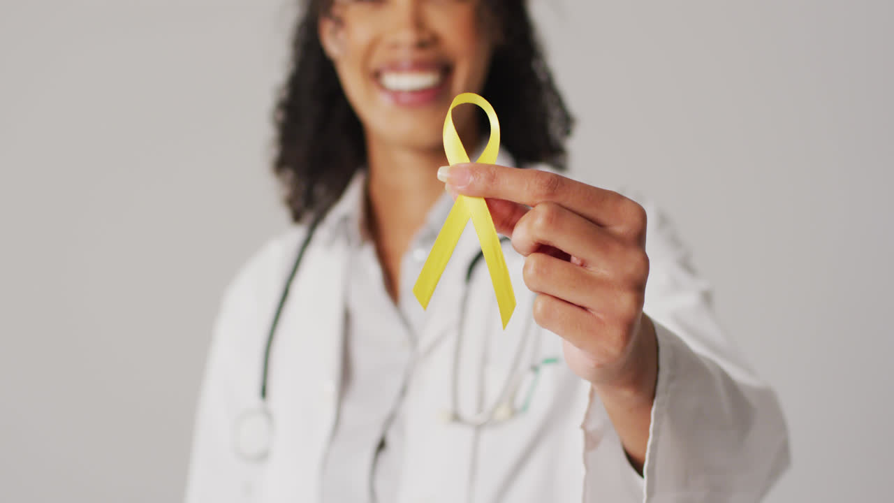 Vídeo de médica birracial sorridente segurando fita amarela de conscientização do câncer de bexiga