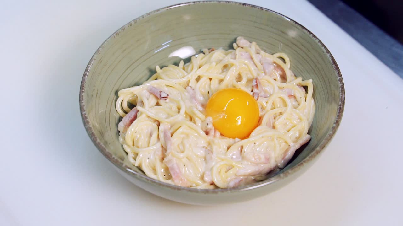Delicious meal. Cook puts raw yolk into cooked pasta with bacon. Professional chef adding egg to creamy spaghetti in a bowl. Restaurant food