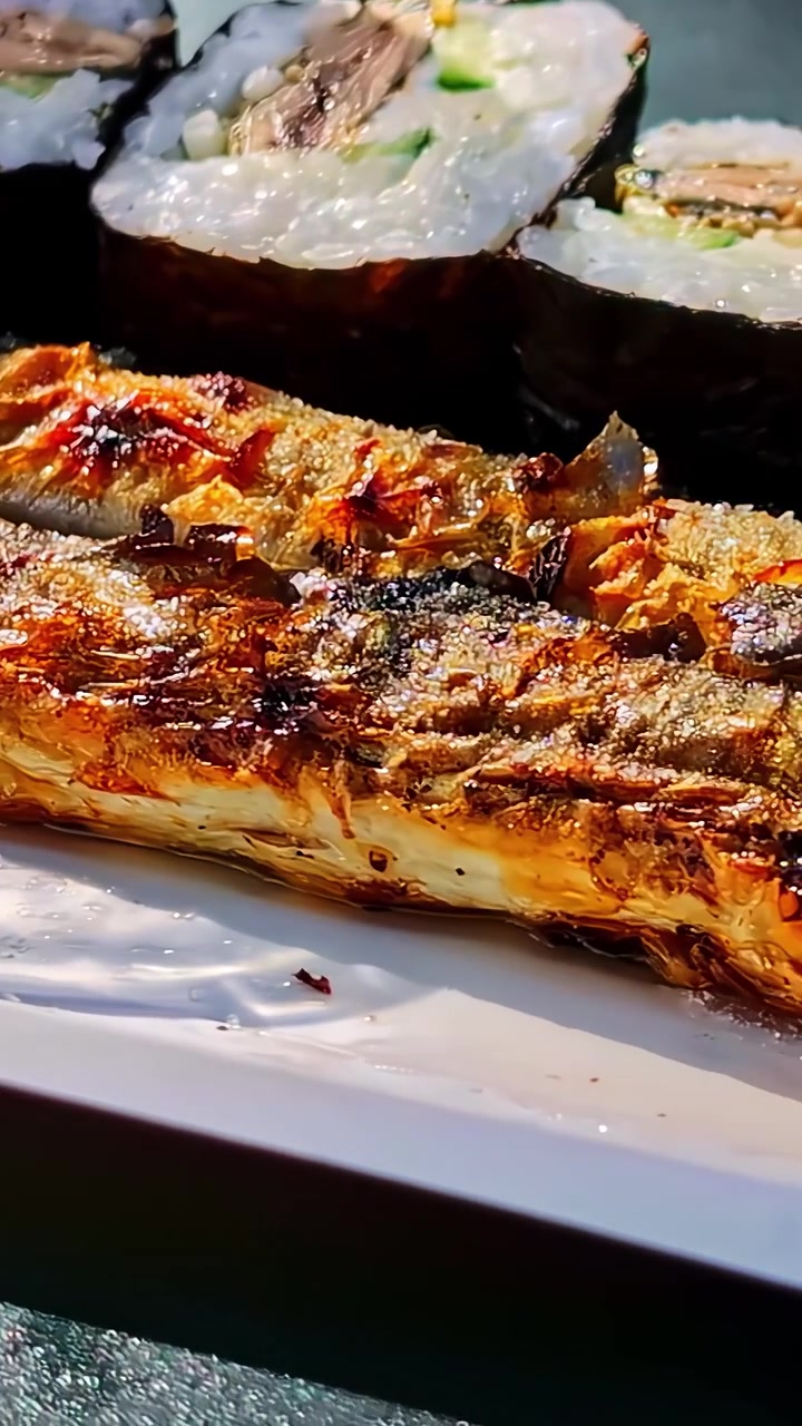 Primo piano verticale di un filetto di pesce grigliato e carbonizzato impiattato con maki roll su un piatto da ristorante