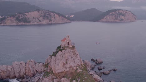 Drone-flying-close-over-famous-Nedjelja-Church-on-rock-during-sunset,-aerial
