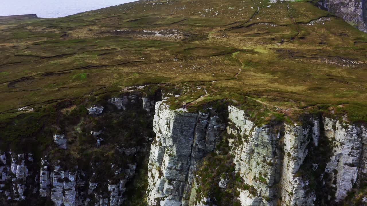 Drone Reverses and Pans Down to Reveal Person Standing on Edge of Horn Head Cliff in Rugged Irish Landscape