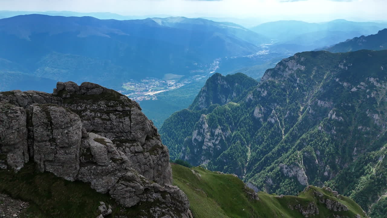 Flight above the huge verdant mountains in Romania. Revealing view on the town located in the valley among the rocks
