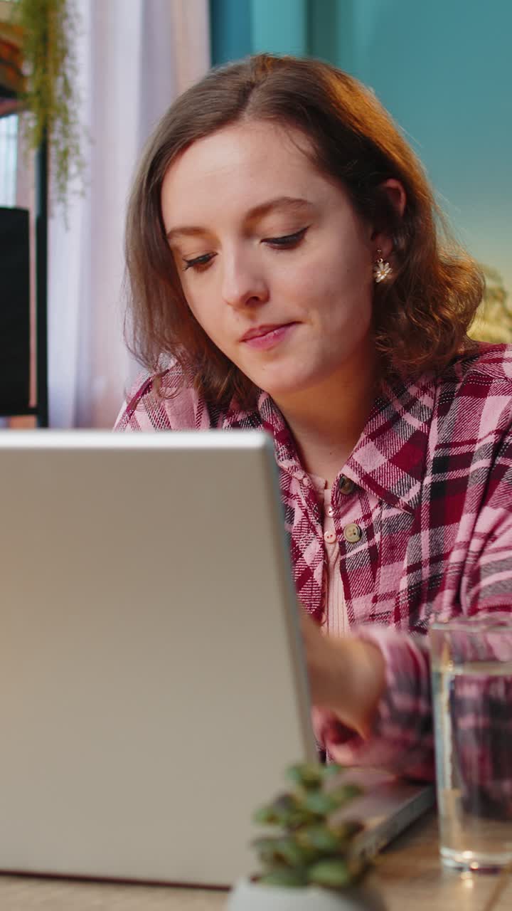Businesswoman girl sitting at workplace desk drinking water while working with laptop in home office