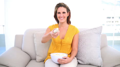mujer sonriente viendo la tv con palomitas de maíz en el sofá