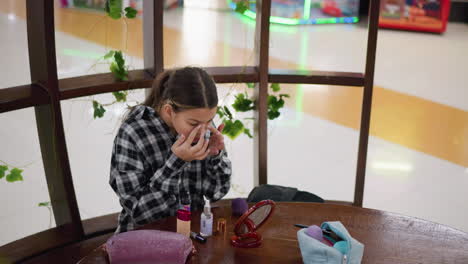 adolescente con camisa a cuadros aplicando maquillaje mientras está sentada en una mesa de madera, productos de belleza, espejo y bolsas de cosméticos están ordenadamente dispuestos, luces interiores vibrantes crean una atmósfera acogedora