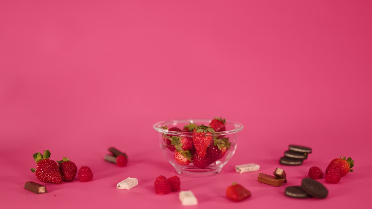 Hand selects chocolate candy from assorted sweets and strawberries on vibrant pink backdrop, studio lighting