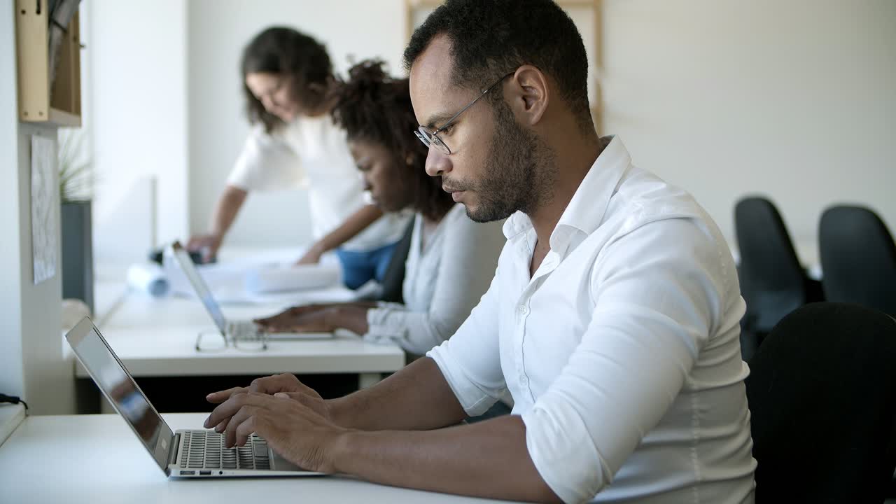 vista lateral de un trabajador masculino enfocado escribiendo en una computadora portátil.