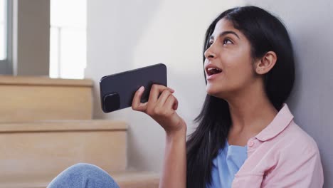 Video-of-happy-biracial-woman-sitting-on-stairs-and-using-smartphone