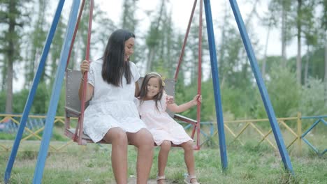 a pregnant mother and her young daughter enjoy playful time together at a playground in the park, surrounded by trees and greenery