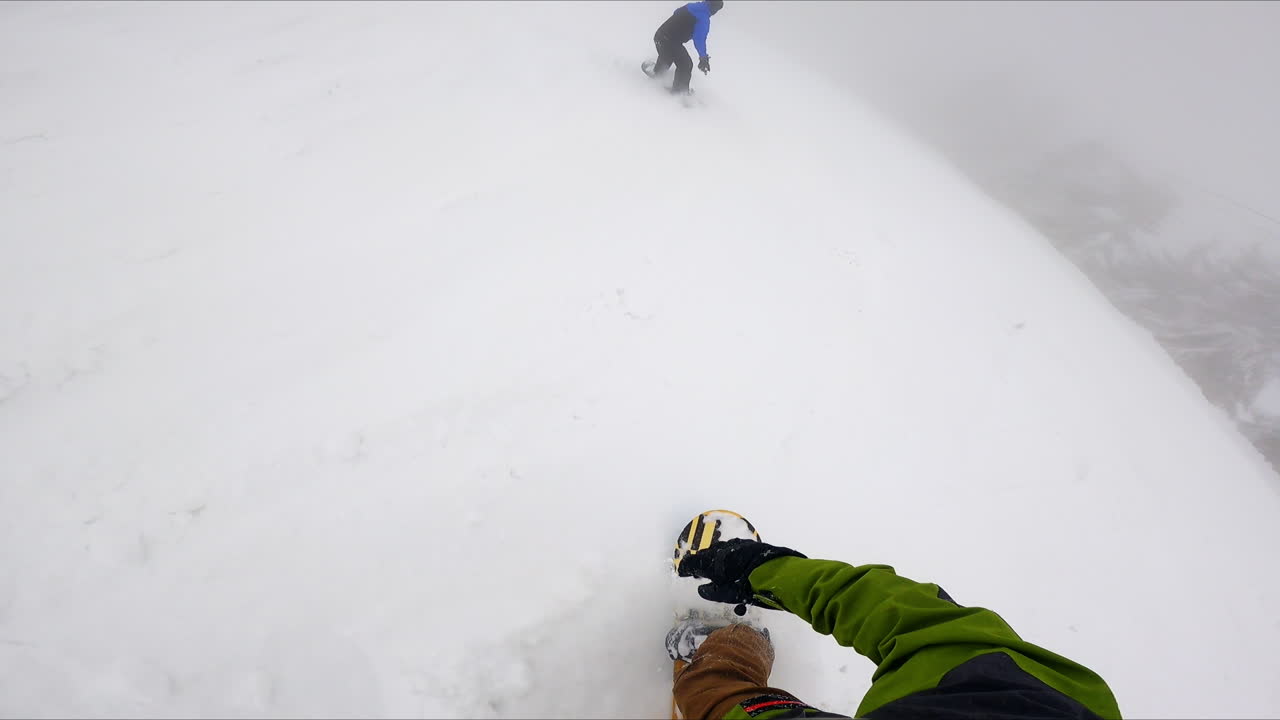 Footage of a person catching up with his fellow sportsman riding ahead. Snowboarding on the snowy day in the mountains.
