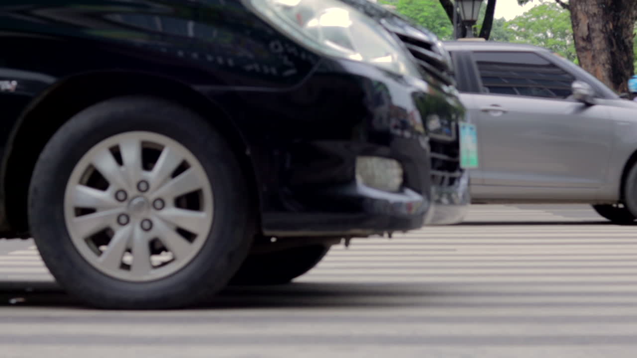 Parking black car at the entrance of a park, as traffic goes by in the background.