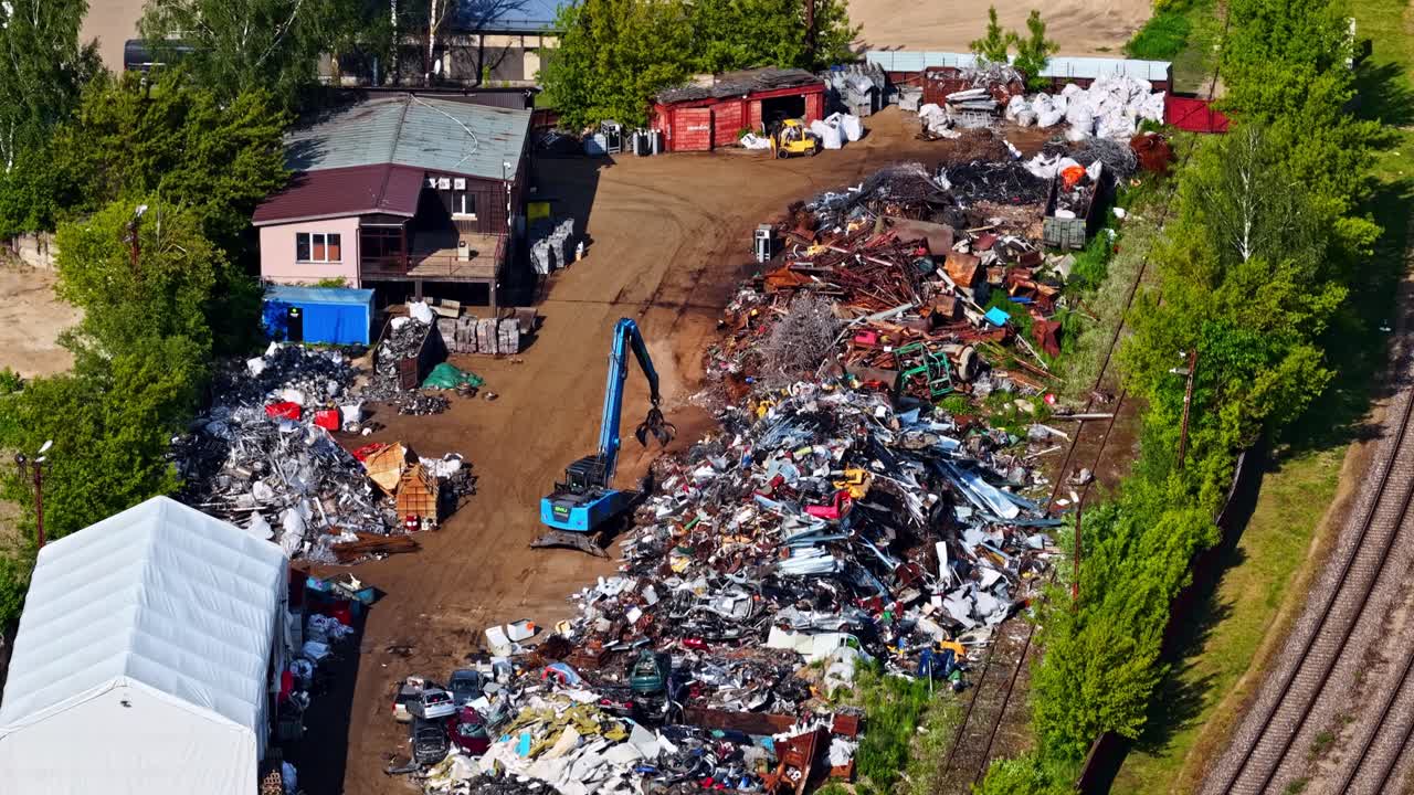 Filmato drone che mostra un grande impianto di riciclaggio di metalli con cumuli di rottami e macchinari pesanti.