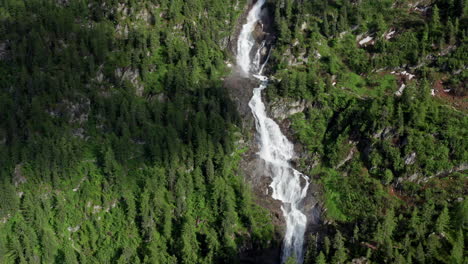 Cascading-waterfall-flowing-through-lush-green-forest-in-Cascate-del-Rutor,-aerial-view