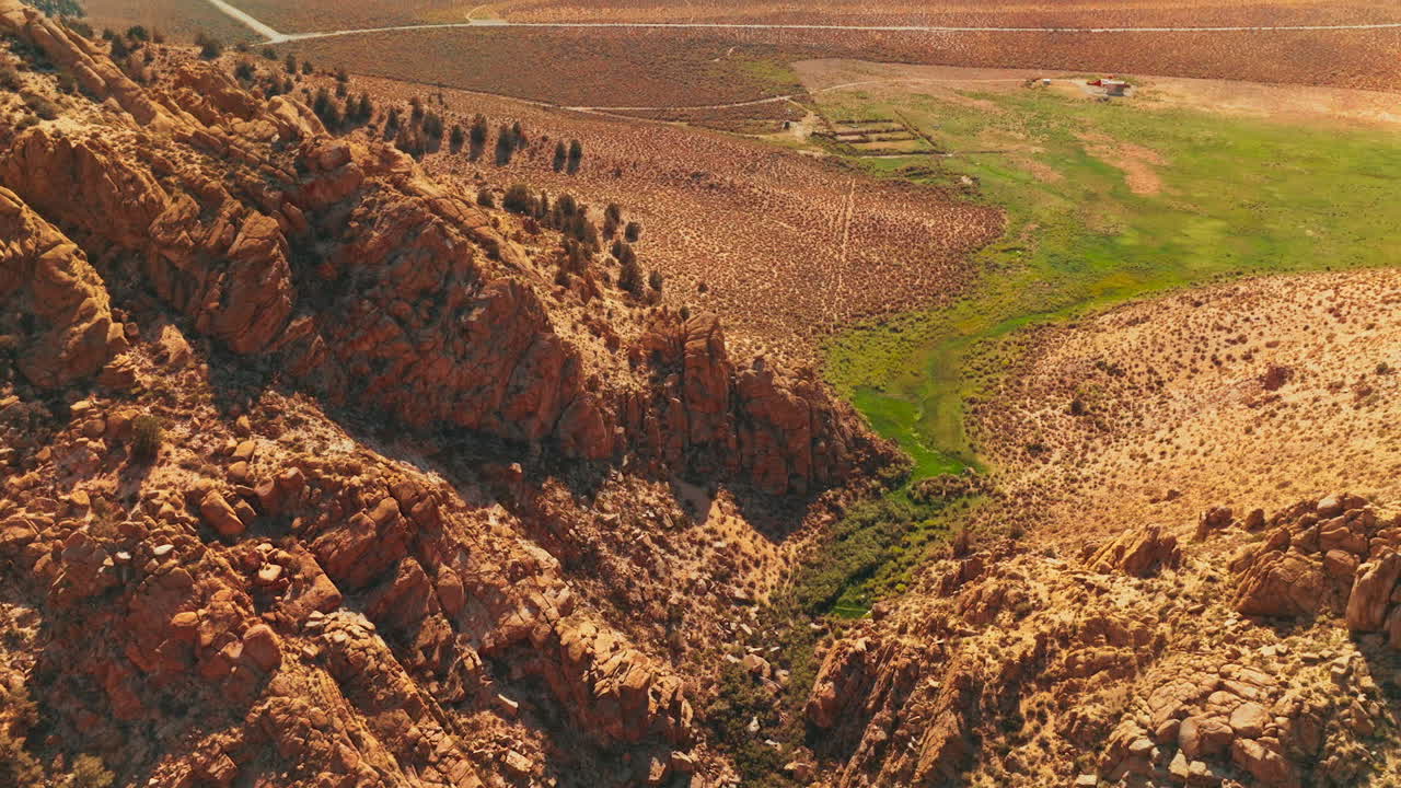 Rising over the crack overgrown with green grass between the mountains. Large rocks of Nevada with desert at foot on sunny day.