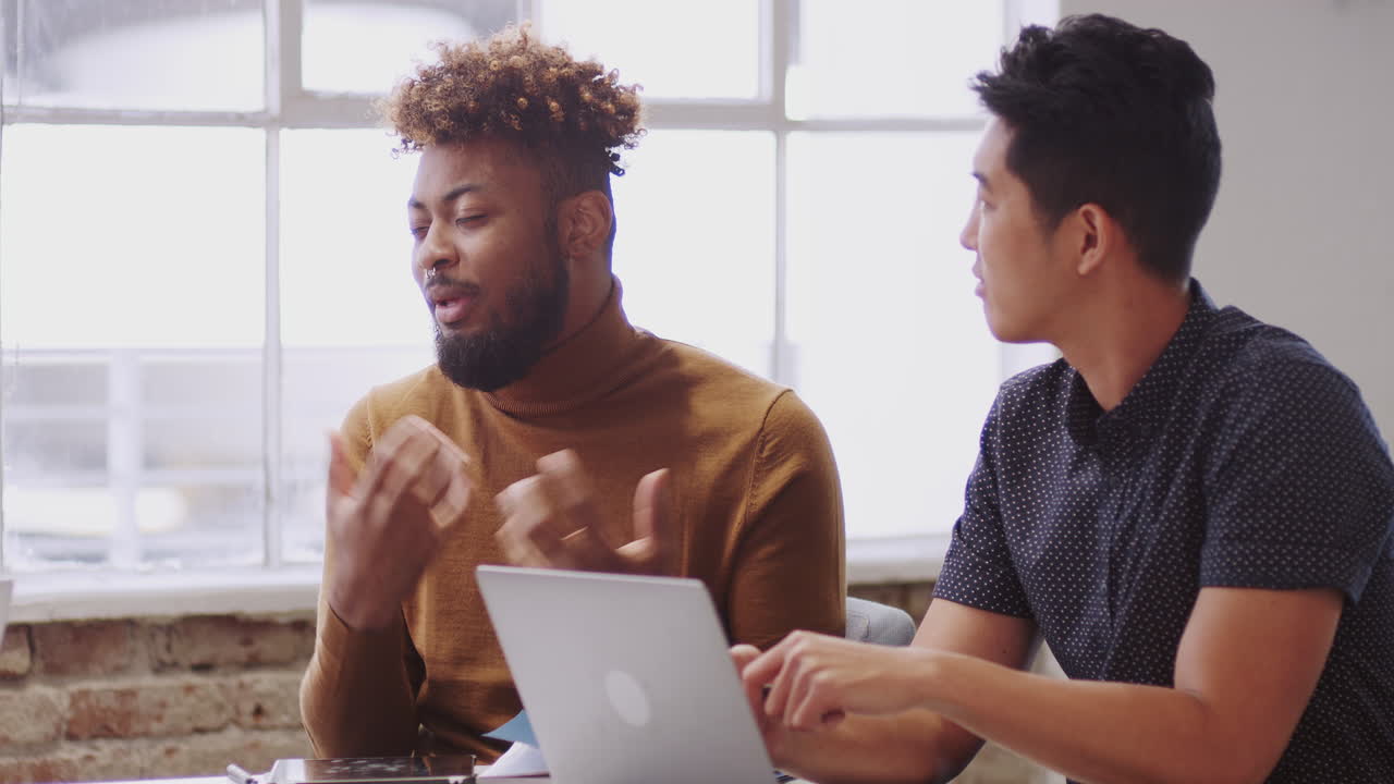 Two male creatives in discussion with an unseen colleague in a meeting room, close up