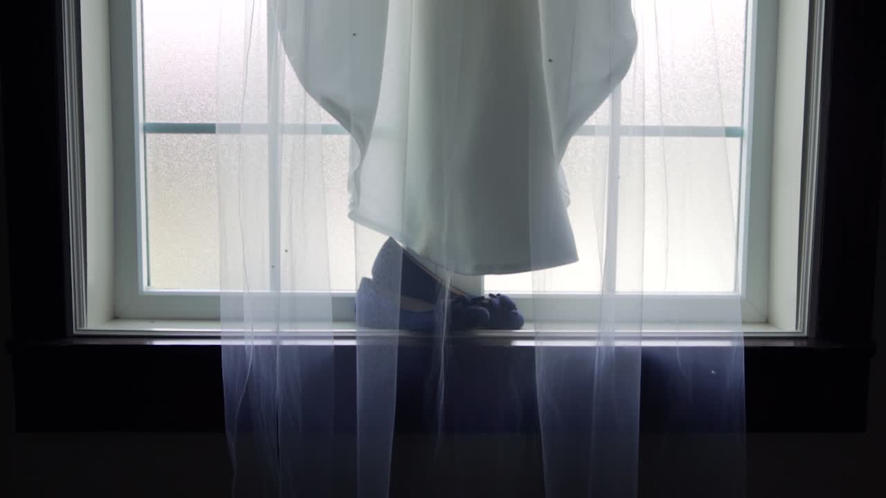 신부의 웨딩 베일과 큰 창턱에 놓인 그녀의 신발 위에 드리워진 드레스의 느린 슬라이더