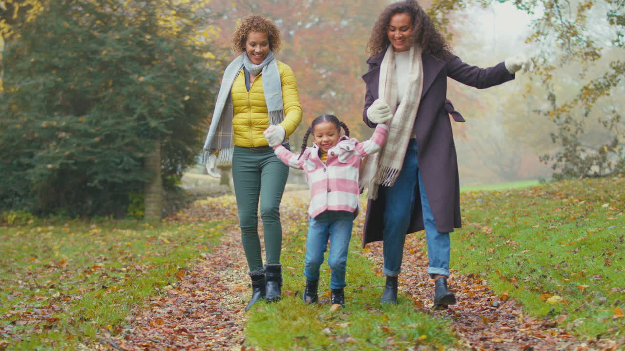 Famiglia femminile multigenerazionale sorridente che cammina e fa dondolare una bambina insieme nella campagna autunnale.