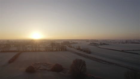 drone flying low over frozen farmlands in the winter at sunrise in the netherlands in 4k