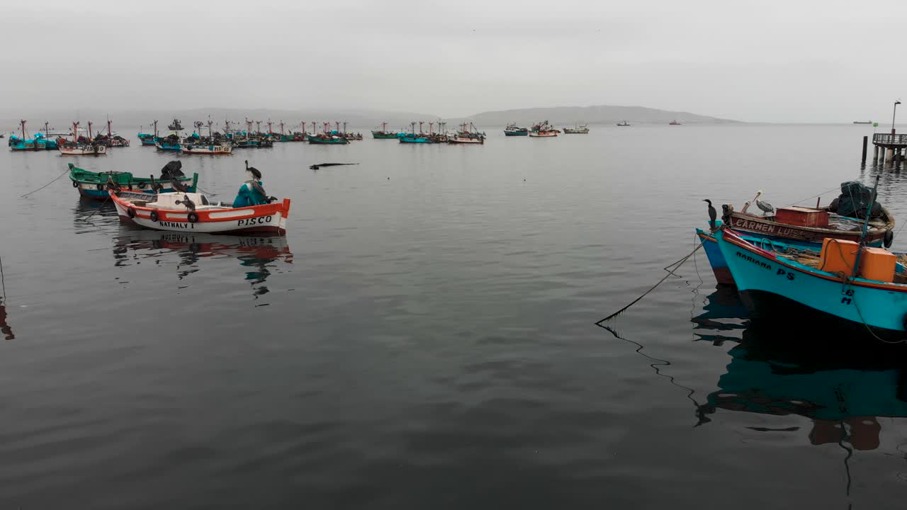 toma aérea mientras la cámara vuela entre barcos de pesca flotando en el océano, cerca de la ciudad de paracas en perú