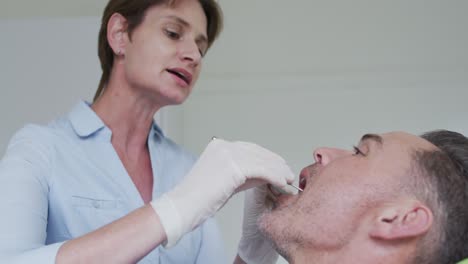 enfermera dental caucásica examinando los dientes de un paciente masculino en una clínica dental moderna