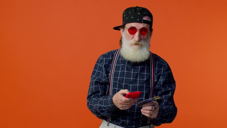 Senior-old-stylish-bearded-man-using-credit-bank-card-and-smartphone-purchases-online-shopping