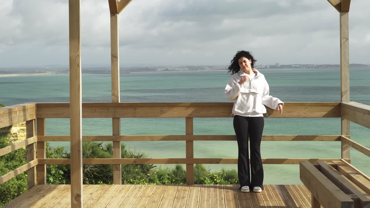 mujer joven relajándose y disfrutando de su viaje turístico observando las vistas frente al océano desde un mirador de madera en la costa del algarve en portugal