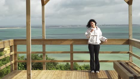 young woman relaxing and enjoying her sightseeing trip watching the ocean front views from wooden lookout on the algarve coast in portugal