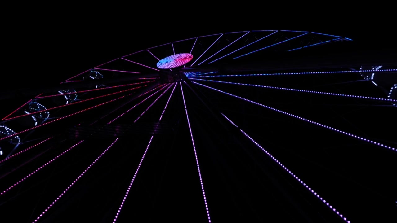Slow motion shot of a ferris wheel turning at night with neon lights