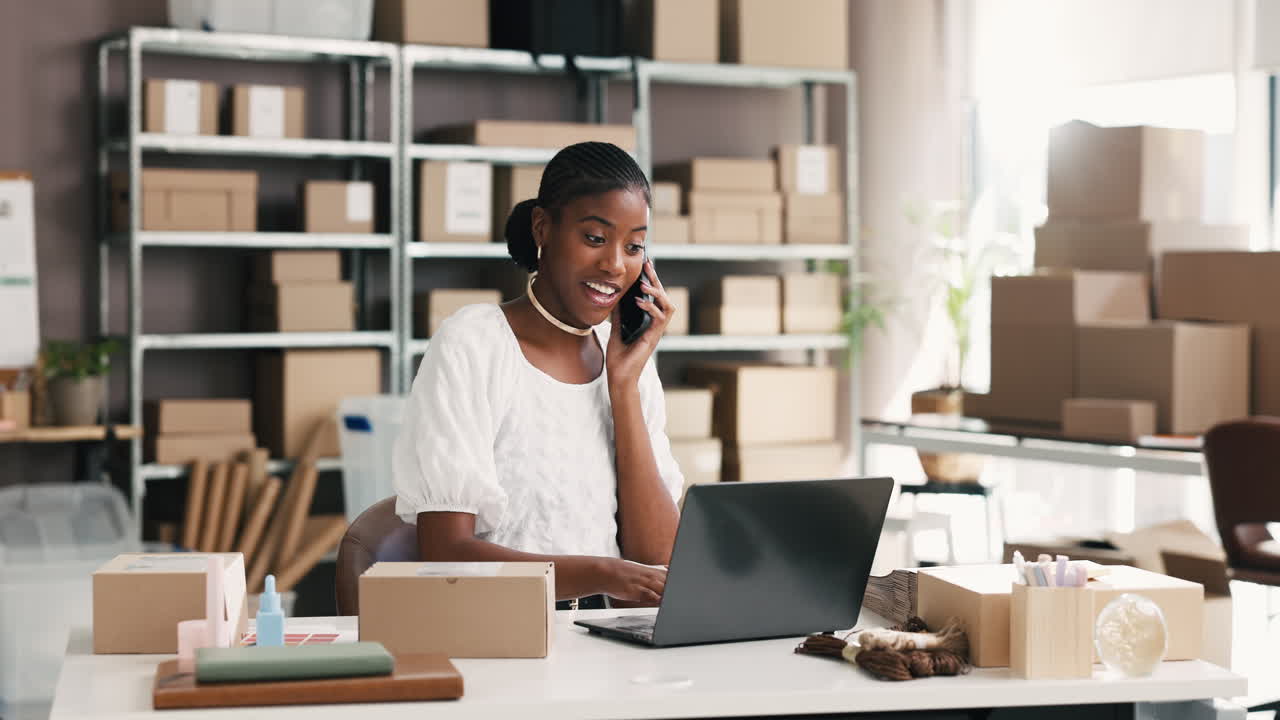 Joven mujer negra hablando por teléfono y trabajando en laptop en una oficina de comercio electrónico