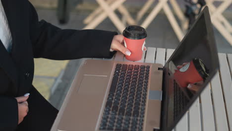 close-up of laptop on table with visible keyboard. person holding tea cup drops it next to laptop and starts typing, fingers adorned with rings, reflection of cup and hand visible on screen