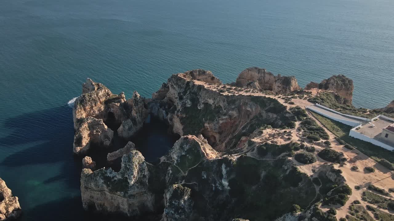 Camera glides forward, tracing iconic coastal arches and golden cliffs as the Atlantic and lighthouse come into view along Portugal’s scenic Algarve coast