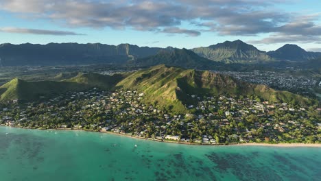 sunrise-panning-drone-aerial-footage-of-lanikai-and-mokulua-islands-vibrant-green-and-blue-tropical-colors-with-steep-mountains-in-background-and-clear-reef-and-ocean-below