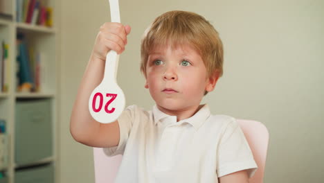 Diligent toddler boy raises tag with digit sitting at desk
