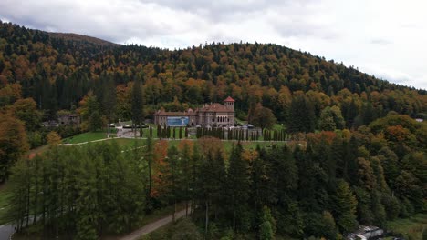 Cantacuzino-castle-amidst-autumn-colored-forests-under-cloudy-skies,-wide-shot,-aerial-view