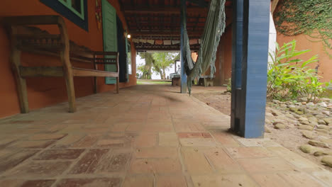 Low-angle-pullback-along-rustic-porch-revealing-wood-bench-and-hammocks-tropical-villa